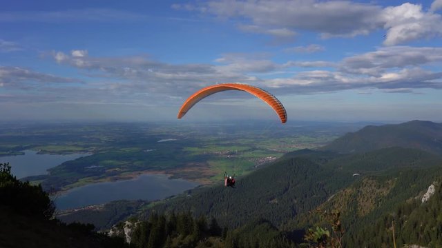 Person paragliding with the instructor in the German Alps mountains with the blue sky and white clouds.