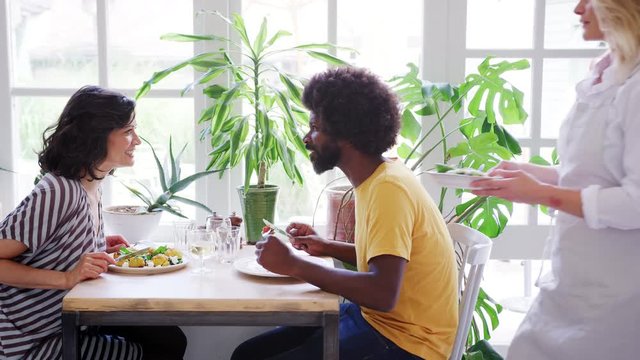Middle aged mixed race couple eating lunch together at a table in a restaurant, a waitress brings them a side dish, close up, side view