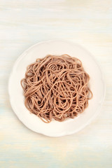 A plate of cooked soba, buckwheat noodles, shot from above on a wooden background with a place for text