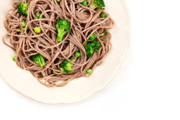 A closeup of a plate of cooked soba, buckwheat noodles with green vegetables, shot from above on a white background with a place for text
