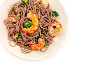 A closeup photo of cooked soba, buckwheat noodles, with shrimps and vegetables, shot from above on a white background with a place for text