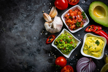 Selection of mexican sauces - salsa, guacamole, cheese sauce and ingredients, dark stone background