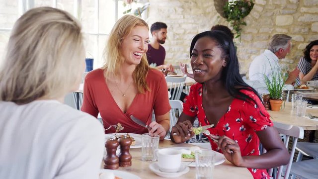 Three young adult women having brunch together and talking in a small restaurant, waist up