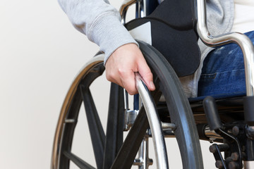 Detail of disabled woman holding a hand on wheel of a wheelchair.