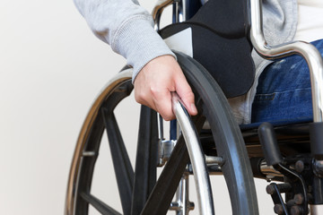 Detail of disabled woman holding a hand on wheel of a wheelchair.