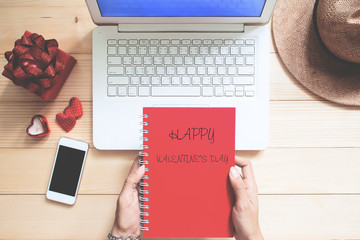 Happy Valentine's Day concept. Woman holding red colour diary on workspace desk with gift box