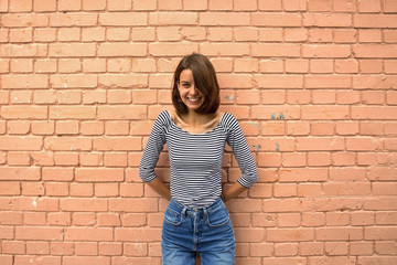 The girl is happy and smiling against the brick wall. Copy space, close up.