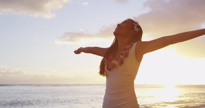 Praising happy freedom woman on beach wearing lei and dress stretching arms up, enjoying sun in worship and meditation zen. Serene girl seen from backside on Hawaii, USA. RED EPIC SLOW MOTION.