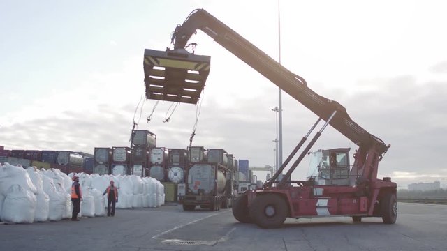 Crane operator and Mobile crane machine stand by waiting for lifting white bags in the dock.