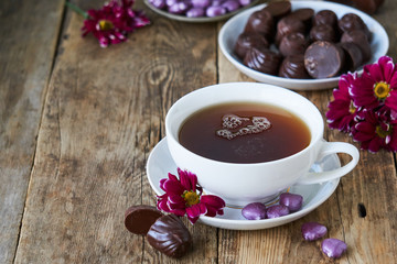 A cup of black tea with candies and flowers on a wooden table