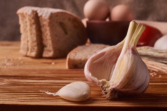 garlic on a wooden table with eggs in clay bowl, tomato, battledore and wheat sprouts
