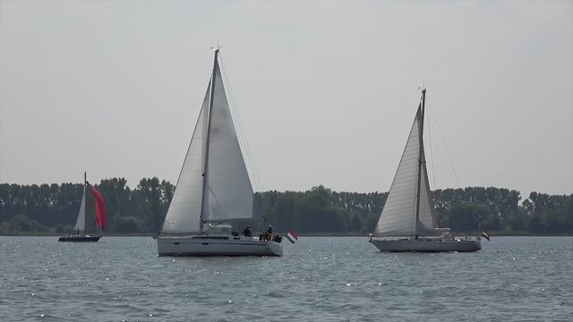 Low angle footage of two sloops racing each other on quiet lake following closely these are small sailing boats with a single mast and a fore and aft rig and one head-sail vessels 4k high resolution
