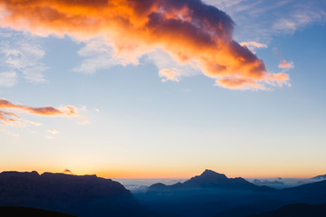 Fototapeta premium Colorful orange clouds in the big blue sky over the dark mountains at sunrise. Beautiful morning landscape in the Caucasus Mountains. Republic of North Ossetia–Alania, Russia