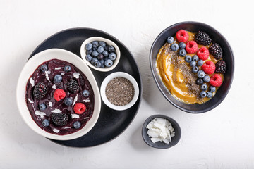 Smoothie bowls on white background. Delicious berry smoothie topped with coconut flakes and berries (raspberry, blackberry, blueberry). Mango smoothie topped with chia seeds and berries.