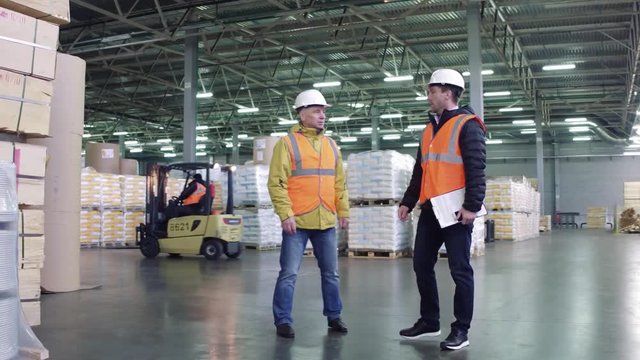 Workers talking , discussing stock inventory standing against tall shelves, copy space.