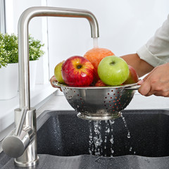 A woman washes fruits by running tap water in the kitchen.