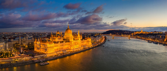 Fototapeta premium Budapest, Hungary - Aerial panoramic view of the beautiful illuminated Parliament of Hungary with Szechenyi Chain Bridge, Buda Castle Royal Palace and colurful clouds at background at sunset