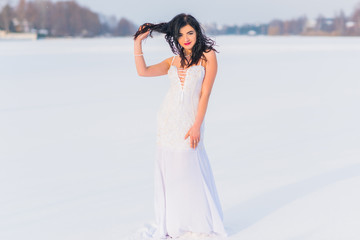 Arabic sexy woman in bright white chiffon long dress at snowy field. Evening fashionable dress,...