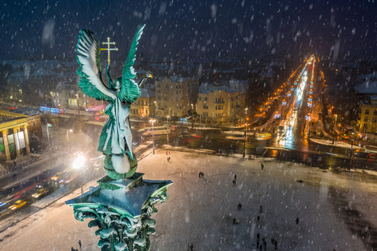 Budapest, Hungary - Aerial view of angel sculpture at Heroes' Square (Hosok tere) with Christmas decorated Andrassy street and trolley bus. Heavy snowing in Budapest