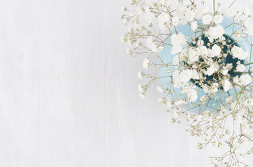 Spring branch with small white flowers in blue sphere vase on white wood table top view, border.