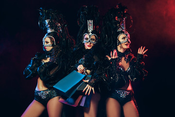 The group of young happy smiling beautiful female dancers with carnival dresses posing with shopping bags on black studio background