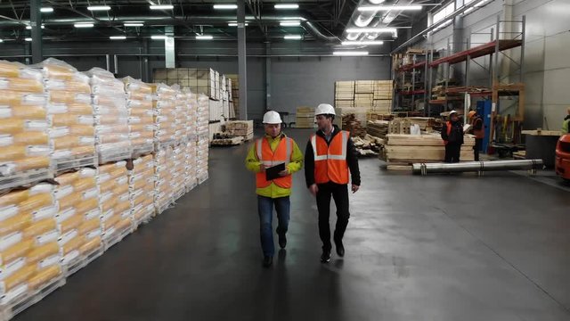 Two workers of warehouse team discussing while walking in warehouse. Aerial, top view.