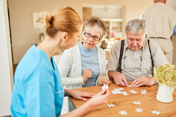 Altenpflegerin hilft Senioren beim Puzzle spielen