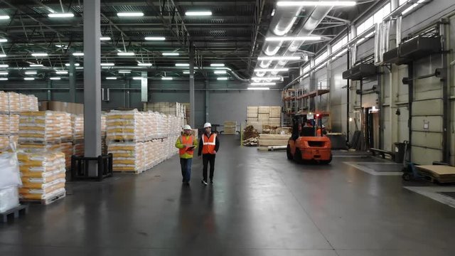 Two workers of warehouse team discussing while walking in warehouse. Aerial, top view.