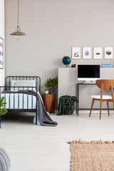 Elegant grey teenager bedroom with single metal bed with blue bedding and grey blanket, real photo with copy space on the empty wall