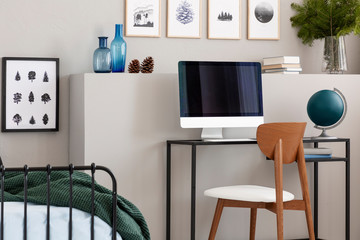 Wooden chair with industrial desk with computer and green globe in elegant teenager room with posters on the grey wall