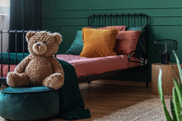Teddy bear on velvet emerald green pouf in fashionable teenager bedroom interior with single bed
