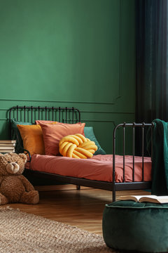 Knot Yellow Pillow On Single Metal Bed With Dark Orange Bedding, Copy Space On Empty Dark Green Wall