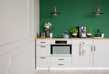 Empty green wall with copy space in elegant kitchen with white furniture,plants and coffee machine