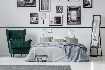 Armchair next to bed with grey pillows in bedroom interior with gallery and mirror. Real photo