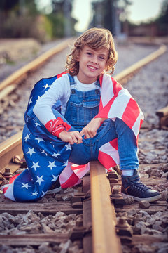Boy sitting on train tracks holding an American flag