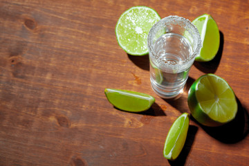 Tequila silver shots with lime slices and salt on wooden board