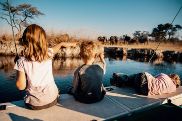 Kinder beobachten Gruppe Elefanten am Ufer des Kwando River bei Sonnenuntergang, Caprivi, Namibia
