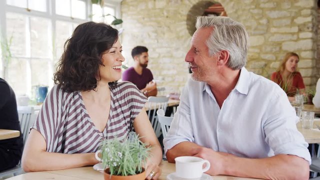 Mature couple laughing and talking while drinking coffee at a table in a restaurant, selective focus