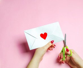 Female hand opens envelope with a red heart. A love letter to the beloved. Valentines day concept. Greeting valentine card. Declaration of love. Wedding invitation. View from above. Flat lay