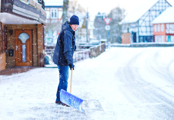 Man with snow shovel cleans sidewalks in winter during snowfall. Winter time in Europe. Young man...