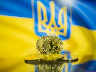 Bitcoin gold coin and defocused flag of Ukraine background. Virtual cryptocurrency concept.