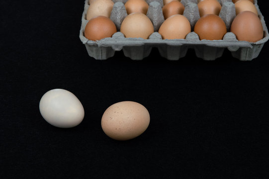 Two chicken eggs on black mat background with a carton box full of eggs