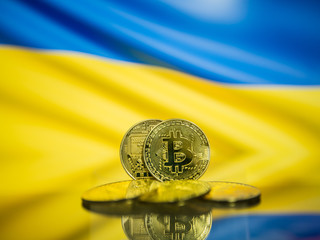 Bitcoin gold coin and defocused flag of Ukraine background. Virtual cryptocurrency concept.