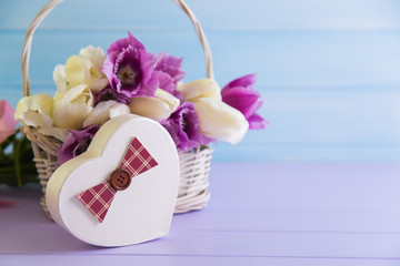 Gift box in form of heart with basket full of purple and white tulips on tender wooden background.