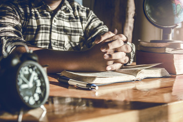 Close up hands of young male praying on wooden table at home in morning time. christian concept.