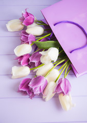 Beautiful bouquet of tender purple and white tulips in shopping bag on lilac wooden background.