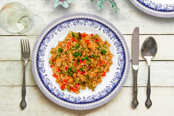 Typical Spanish and Andalusian rice with vegetables served on a rustic wooden table next to some white wine and floral decoration. Top view and empty copy space for Editor's text.