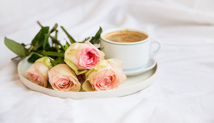 Obraz na płótnie Canvas Bed coffee cup with roses bouquet, romantic bed breakfast with flowers and cappuccino coffee cup
