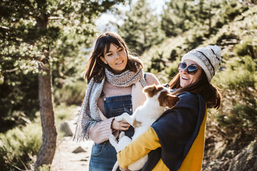 Fototapeta premium .Two good friends walking through the mountains on a sunny winter day, accompanied by their sweet brown and white dog. Dogfriendly. Lifesytle.