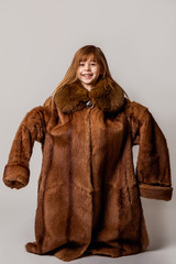 Vertical portrait of a child in a silly mood. Posing in a large natural coat with a fur collar....